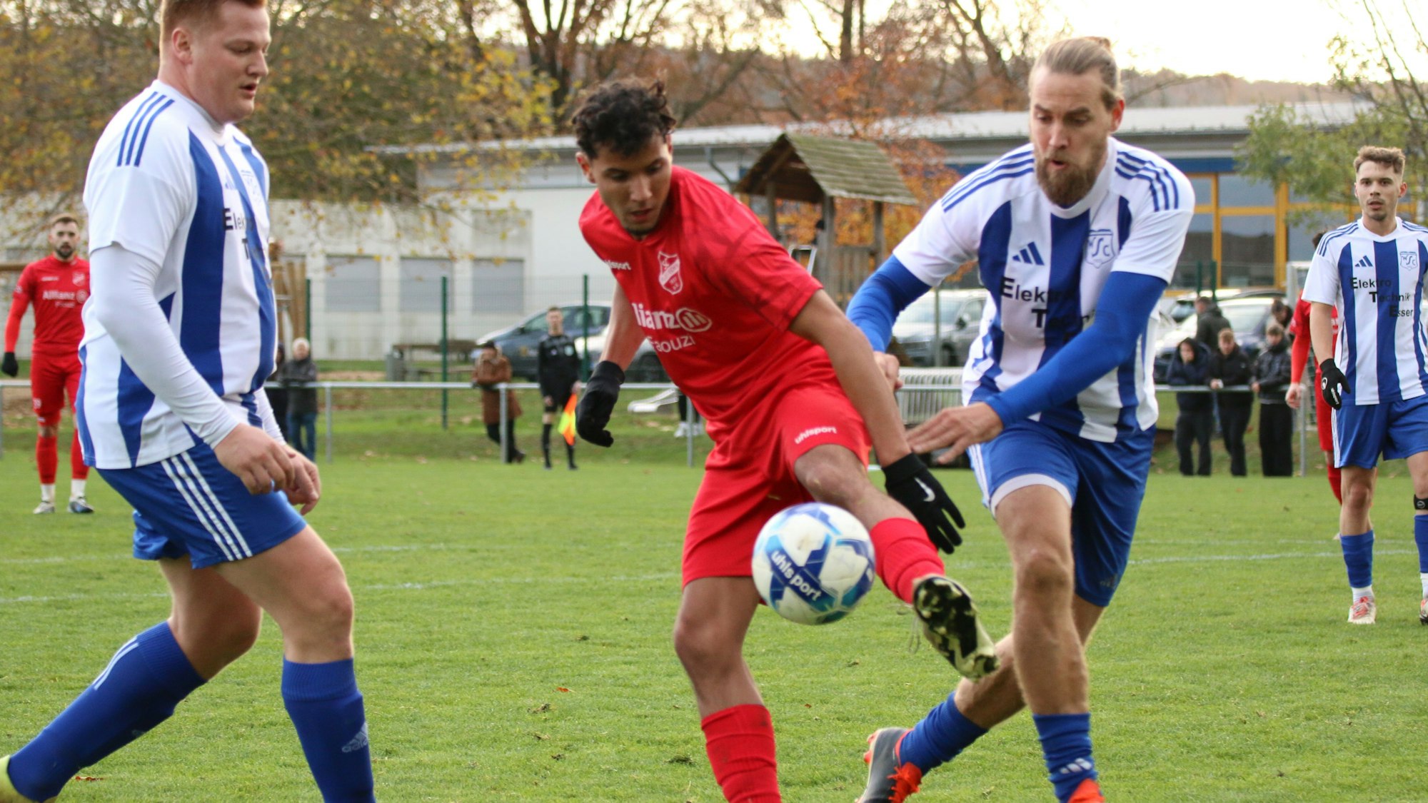 Ein Fußballer behauptet den Ball, obwohl er von zwei Verteidigern bedrängt wird.