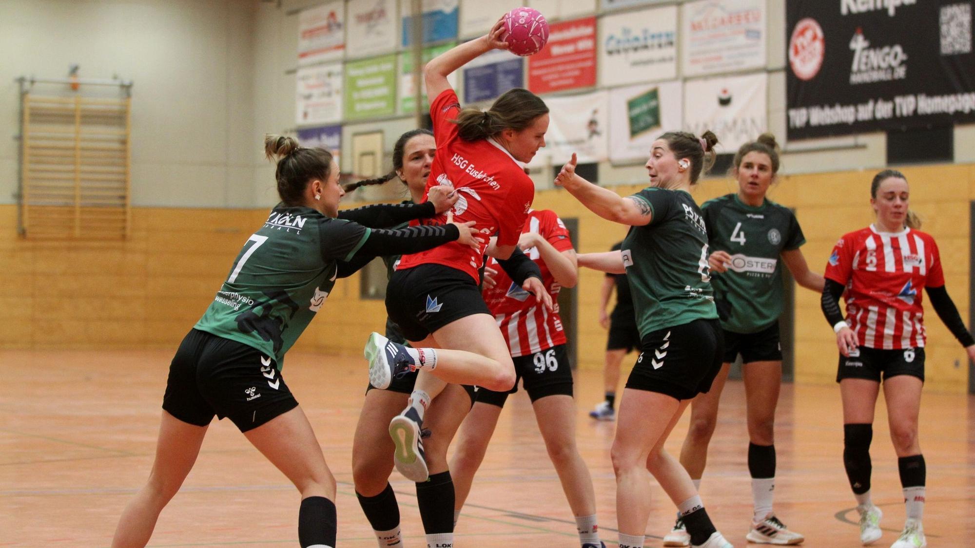 Eine Handballerin steigt zum Wurf hoch und wird dabei von gleich drei Gegenspielerinnen bedrängt.