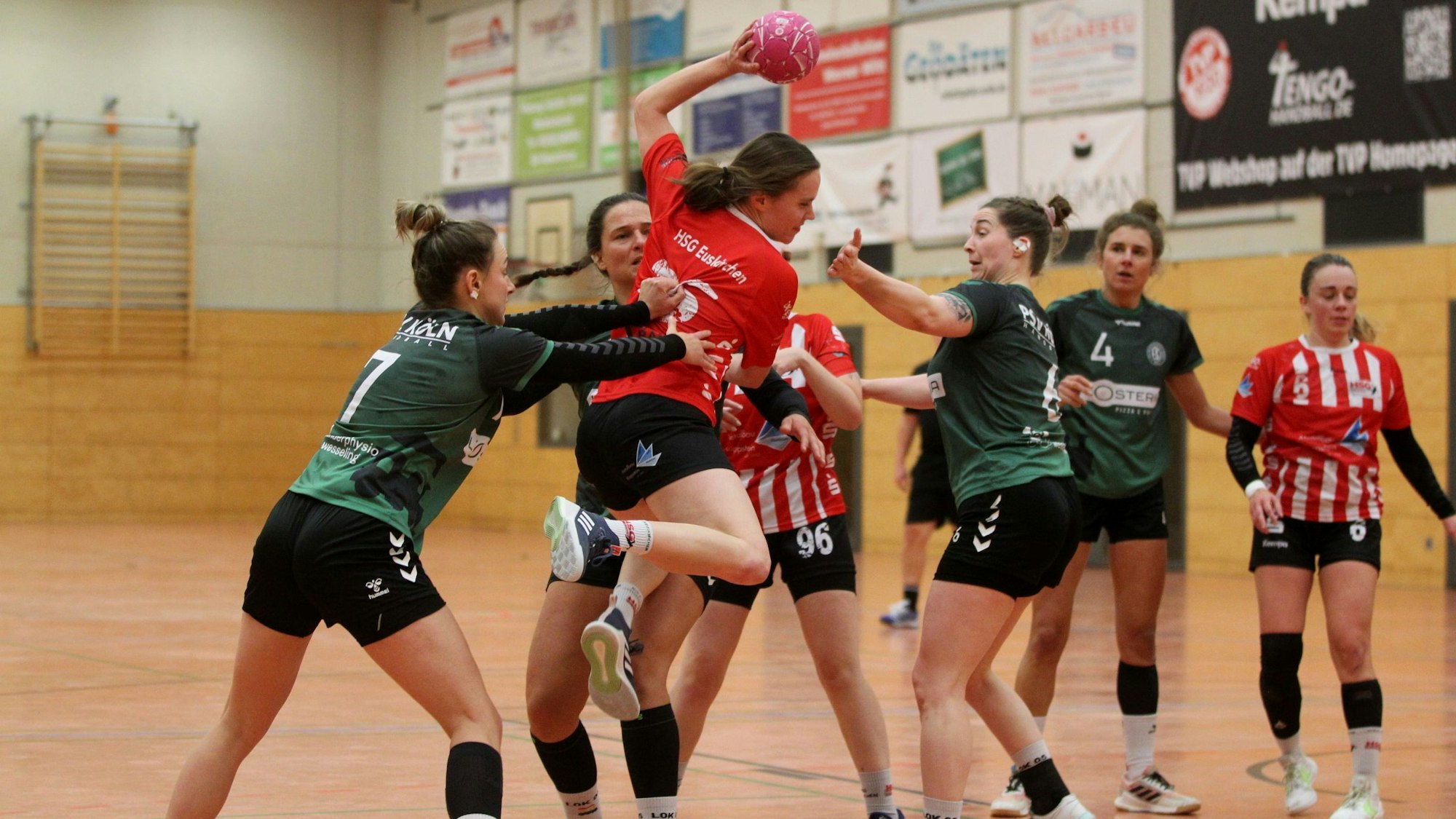 Eine Handballerin steigt zum Wurf hoch und wird dabei von gleich drei Gegenspielerinnen bedrängt.