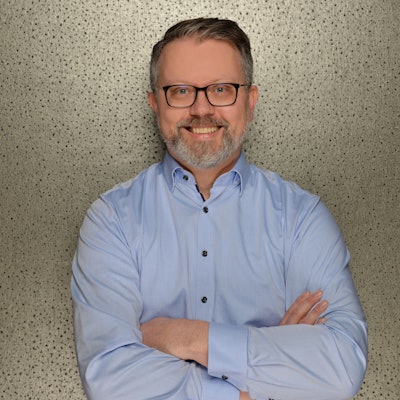 Ein Mann steht vor einer Wand und lächelt.