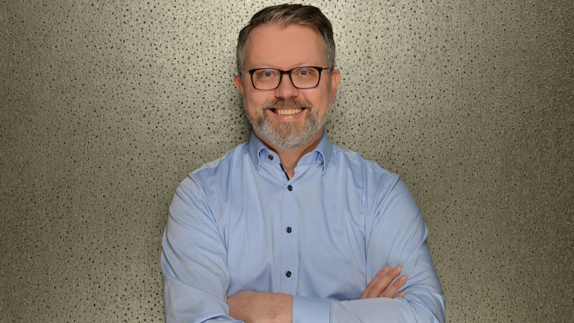 Ein Mann steht vor einer Wand und lächelt.