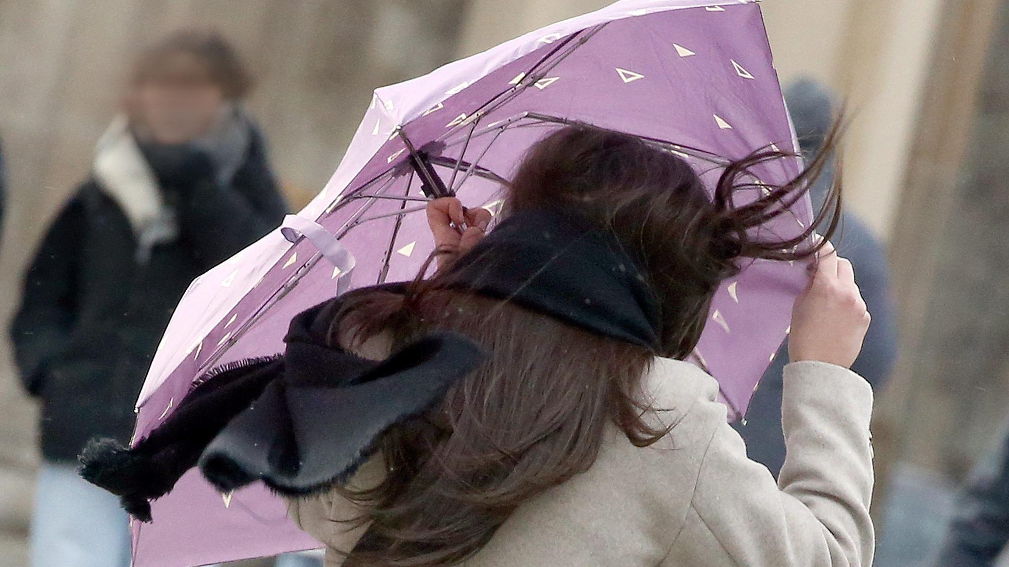 Eine Passantin mit wehenden Haaren sichert ihren Regenschirm, während sie sich bei Windstärken bis 100 km/h vor dem Brandenburger Tor entlang spaziert.