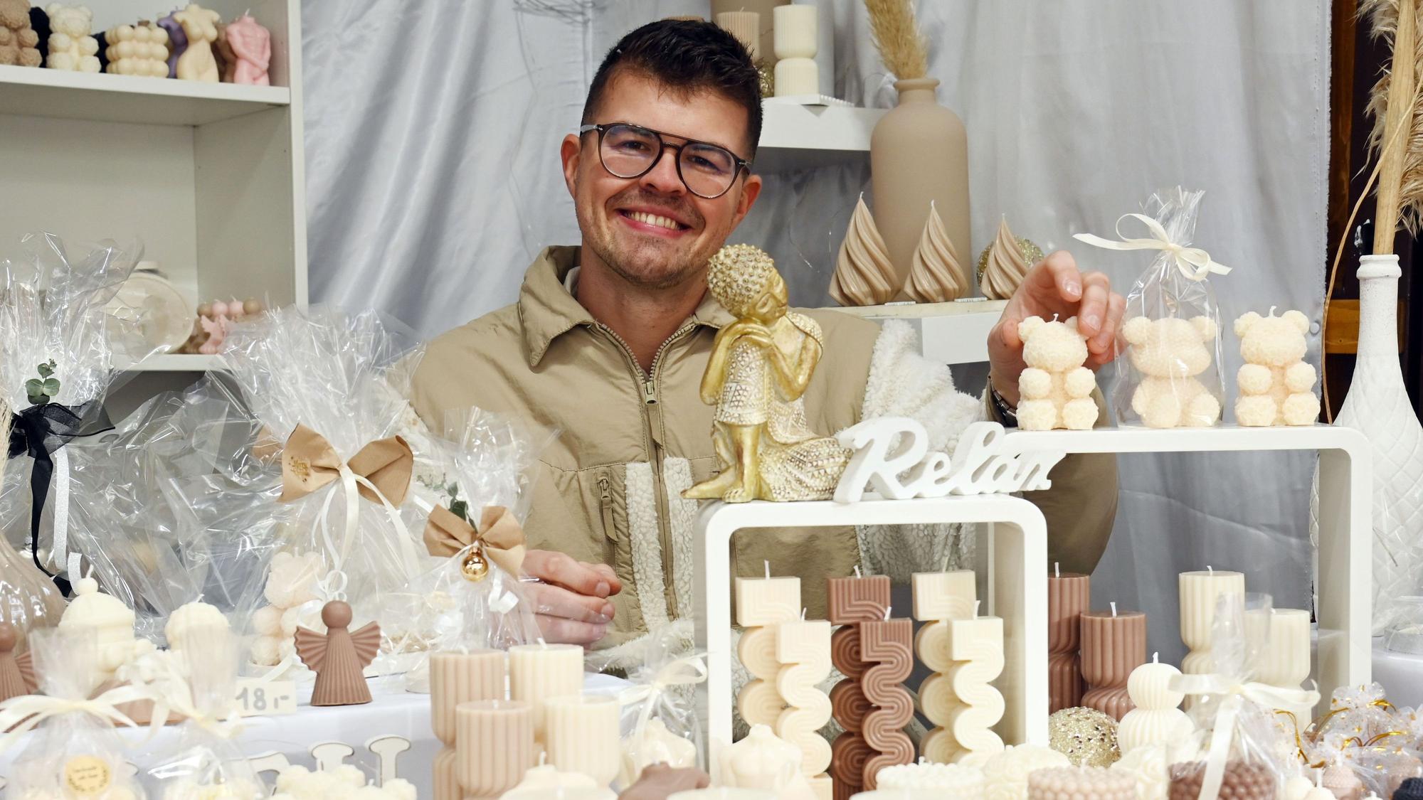 Max Münsterkötter von „Lichtgestalt “sitzt hinter verschiedenen Kerzen auf dem Weihnachtsmarkt am Rudolfplatz.