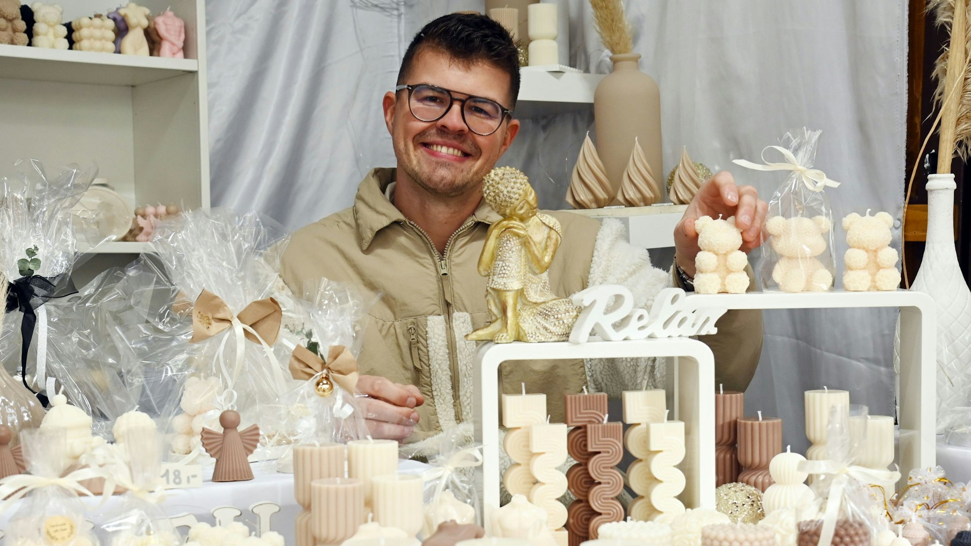 Max Münsterkötter von „Lichtgestalt “sitzt hinter verschiedenen Kerzen auf dem Weihnachtsmarkt am Rudolfplatz.