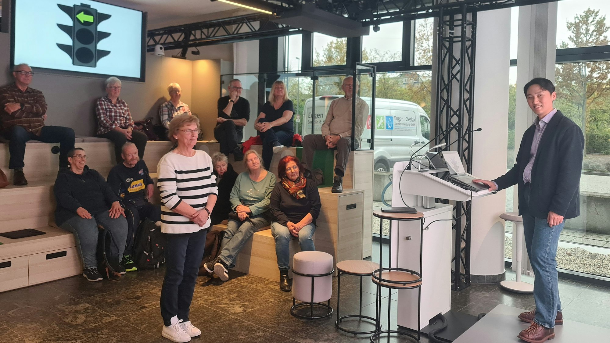 Zu sehen ist Dr. Kim, der auf einer Bühne an einem Rednerpult steht, sowie mehrere Teilnehmerinnen und Teilnehmer des Workshops.