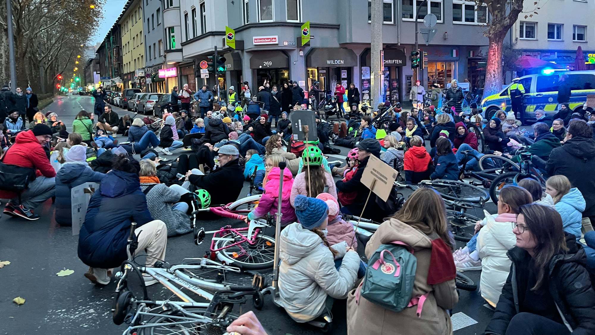 Eine Menschenmenge sitz und liegt auf der Fahrbahn - teilweise mit Schildern und Fahrrädern.