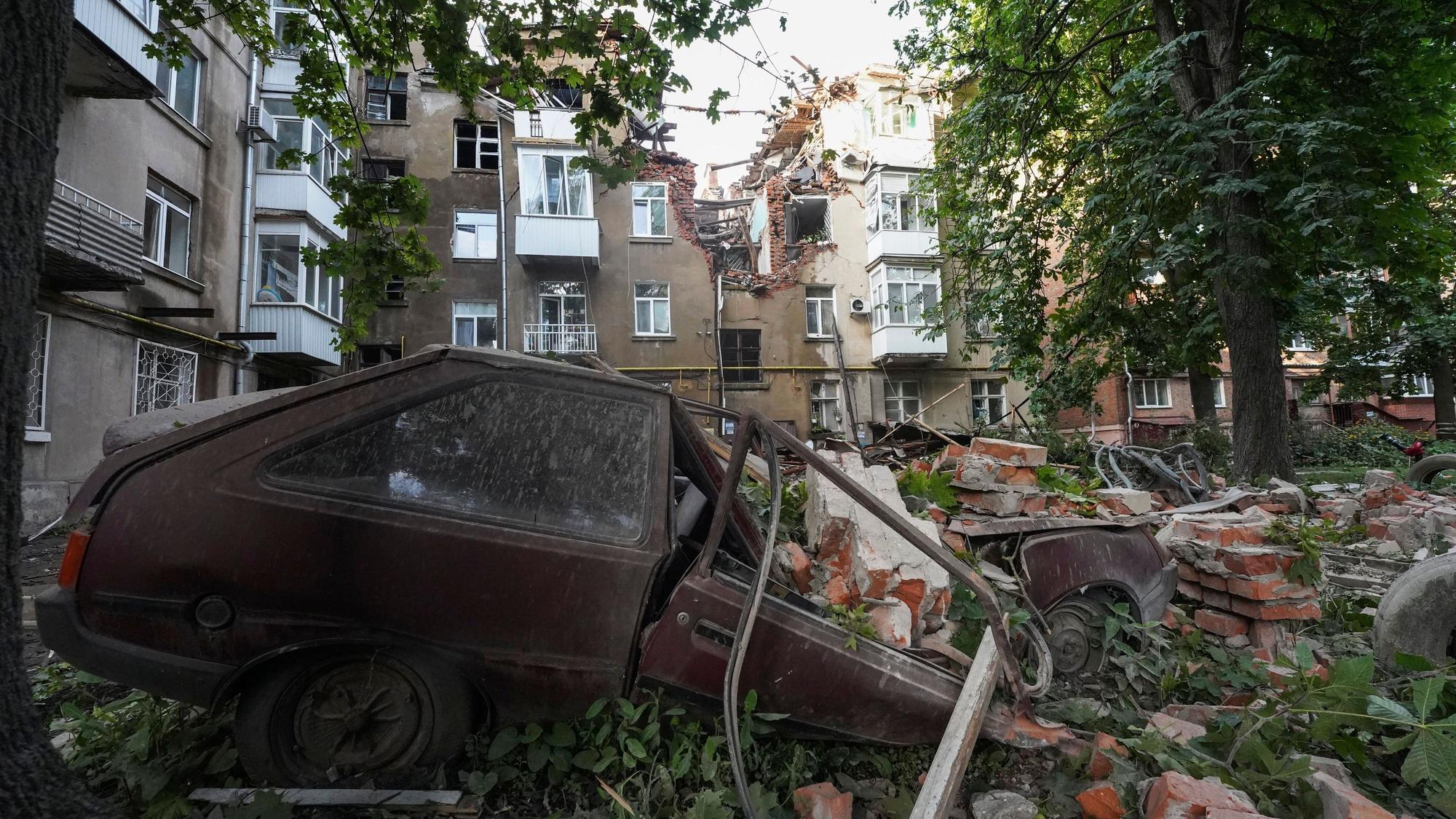 Ein Autowrack ist nach einem Angriff vor einem beschädigten Wohnhaus zu sehen.