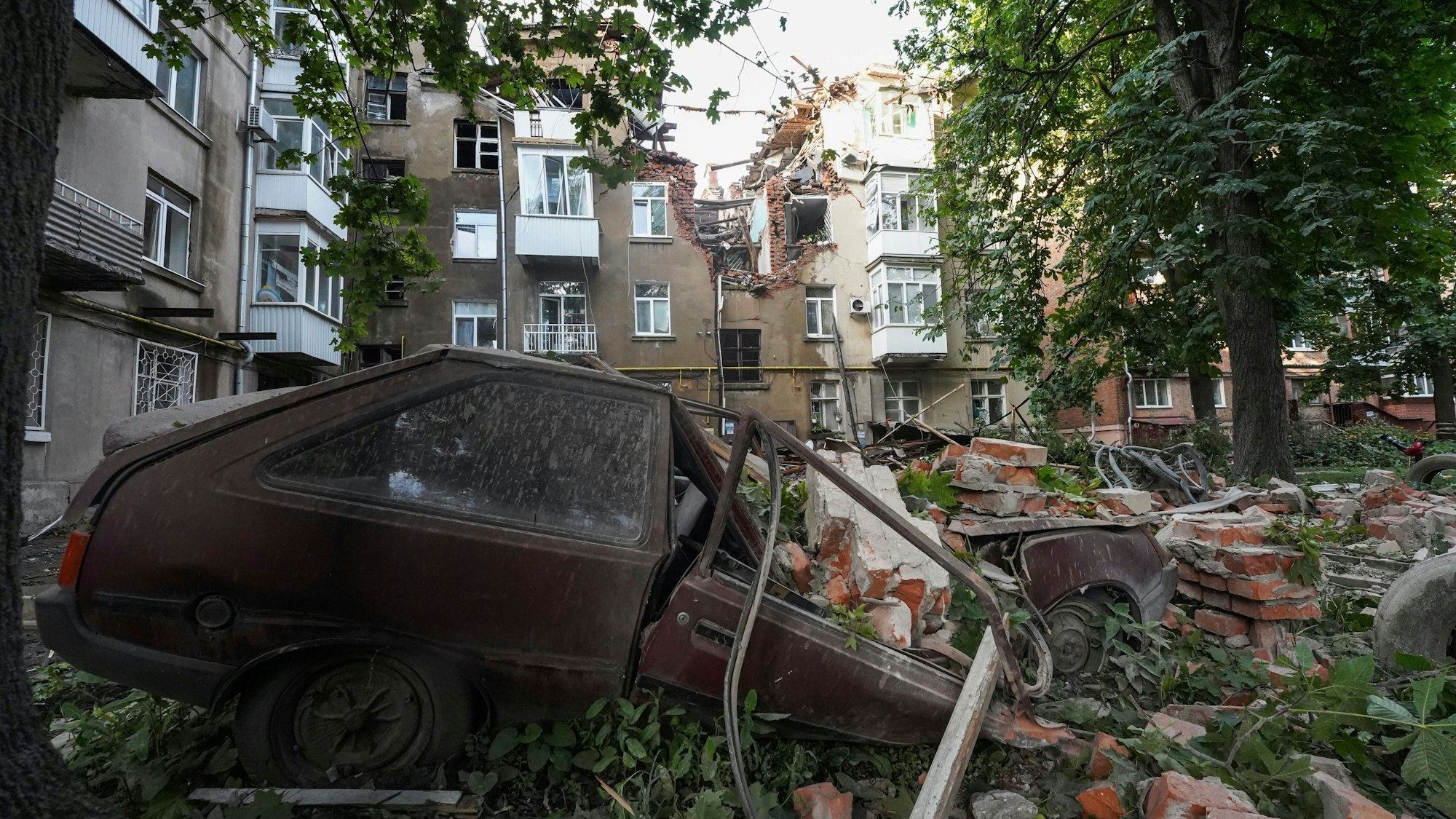 Ein Autowrack ist nach einem Angriff vor einem beschädigten Wohnhaus zu sehen.