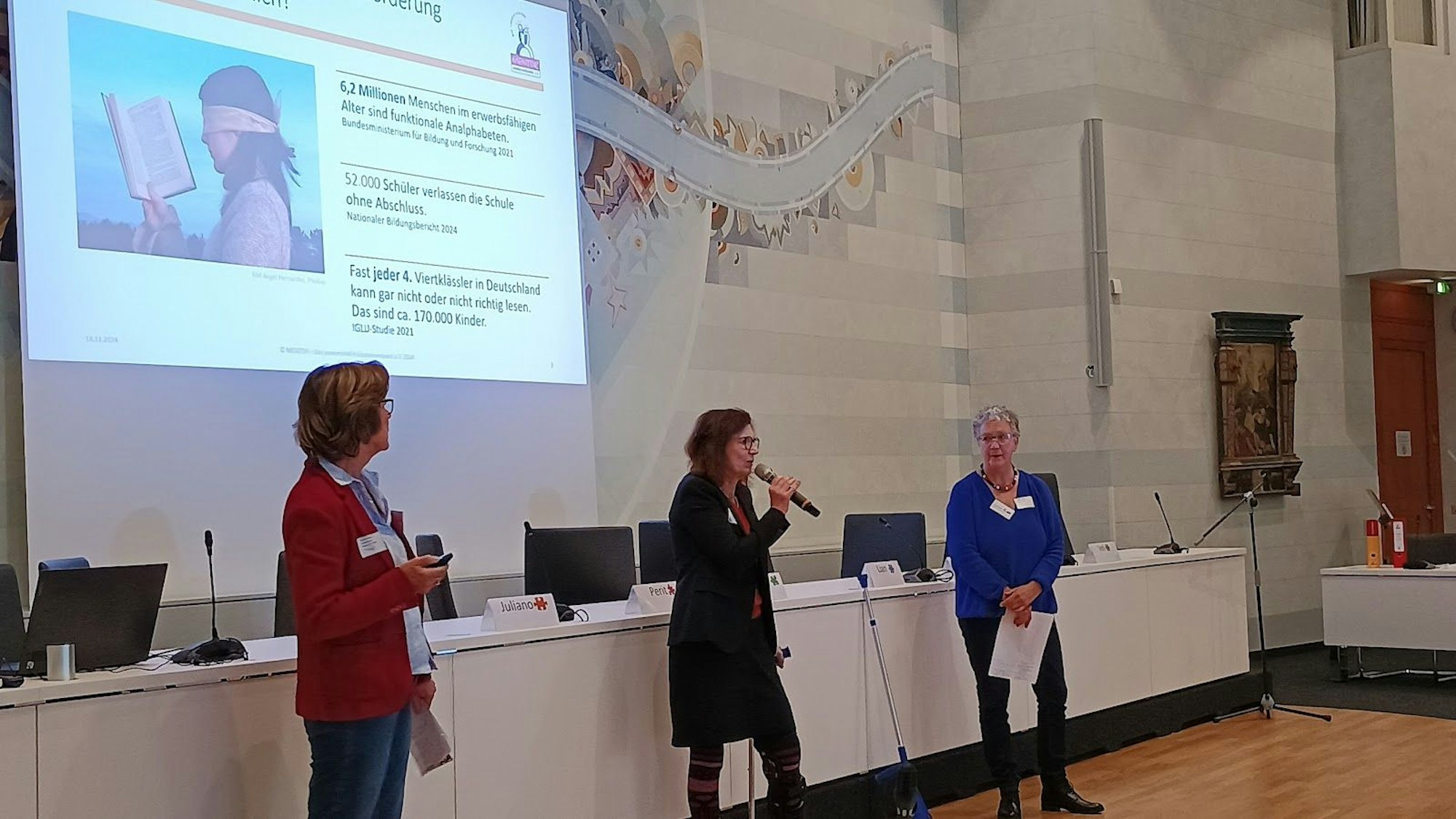 Zu sehen sind drei Frauen vor einer Beamer-Präsentation.