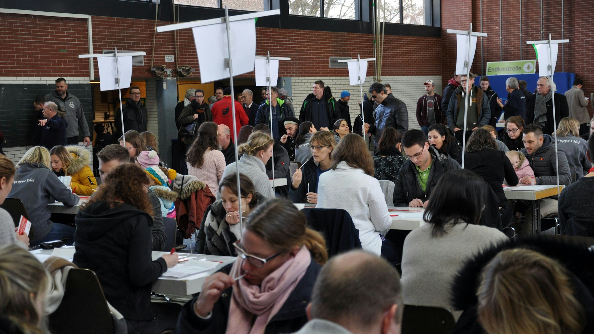 Zahlreiche Menschen sitzen an Tischen in der Sporthalle, um sich typisieren zu lassen.