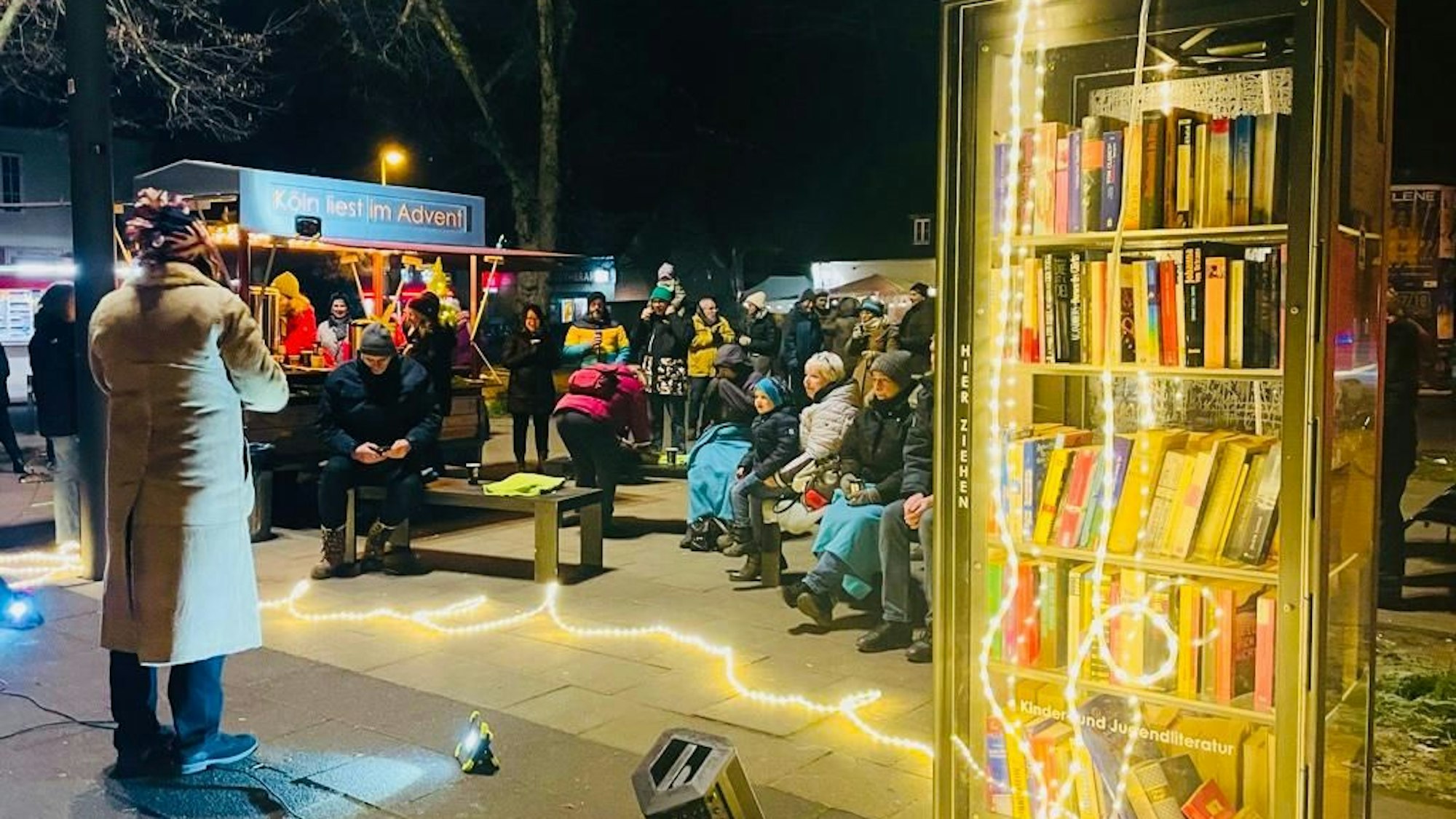 Menschen versammeln sich vor einem weihnachtlich beleuchtetem Bücherschrank in Vogelsang