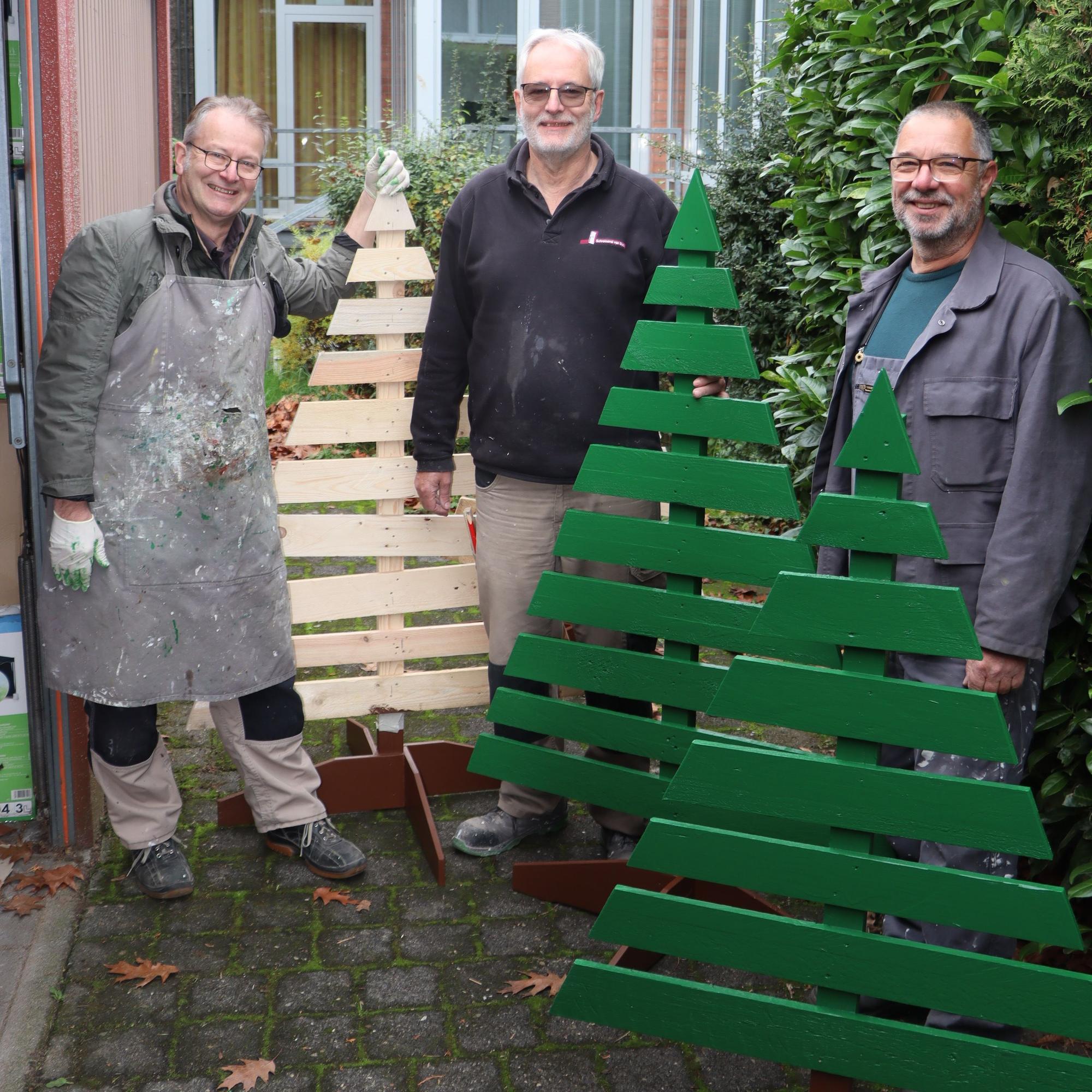 Auf dem Bild sind drei Männer in Arbeitskleidung und von ihnen gebaute Weihnachtsbäume aus Holzpaletten zu sehen.