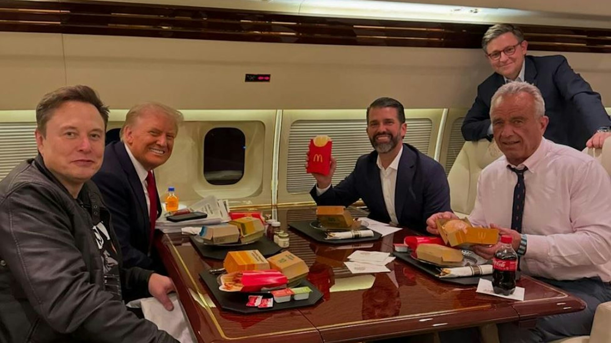 Donald Trump sitzt mit Elon Musk, seinem Sohn Donald Trump Jr. und Robert Kennedy Jr. in seinem Privat-Jet und freut sich auf sein Fast-Food-Menü.