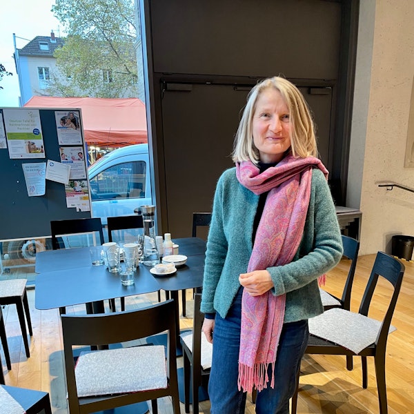 Frau Ocken steht vor einem Tisch im Sprachencafé und lächelt freundlich in die Kamera.