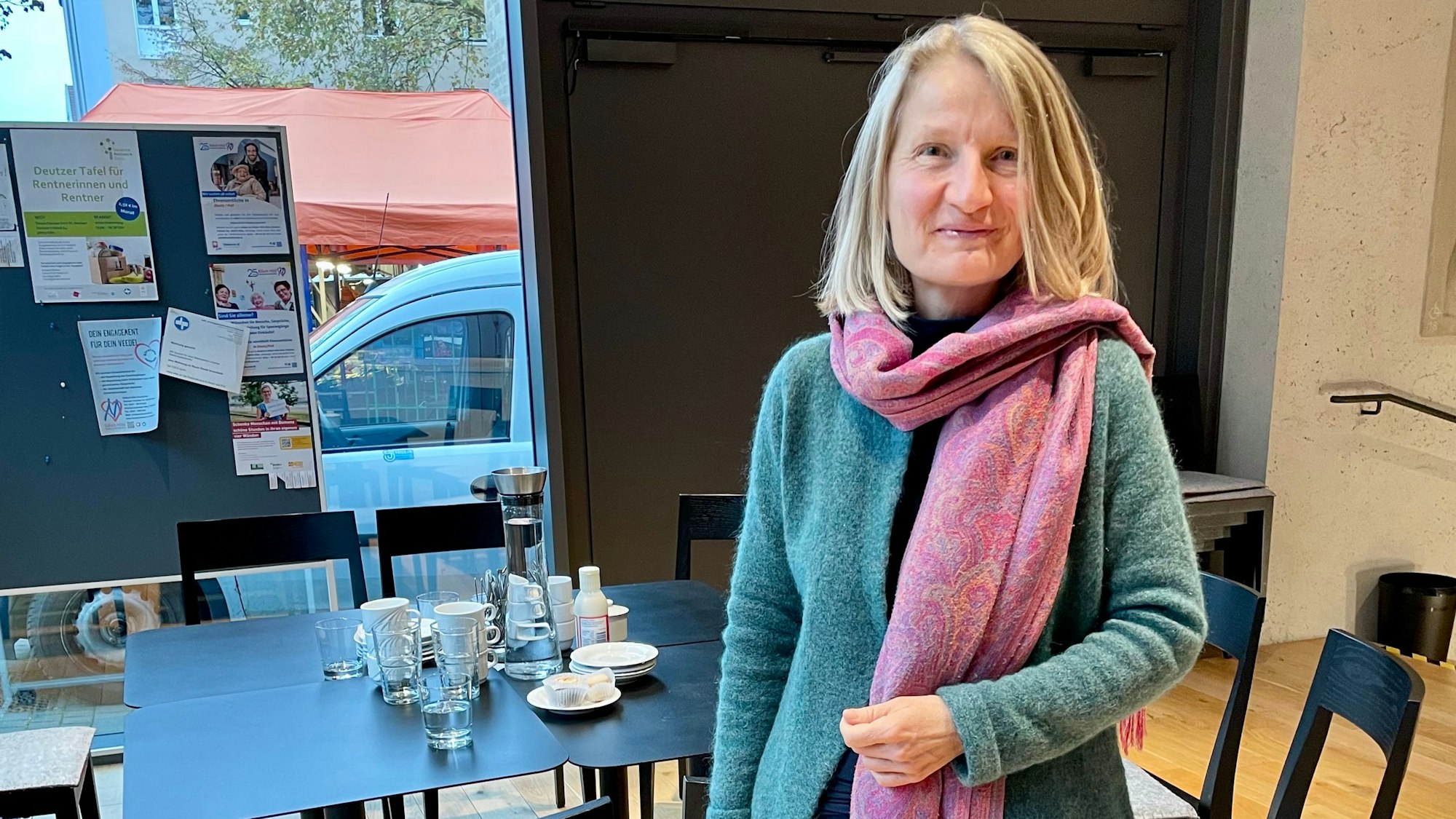 Frau Ocken steht vor einem Tisch im Sprachencafé und lächelt freundlich in die Kamera.