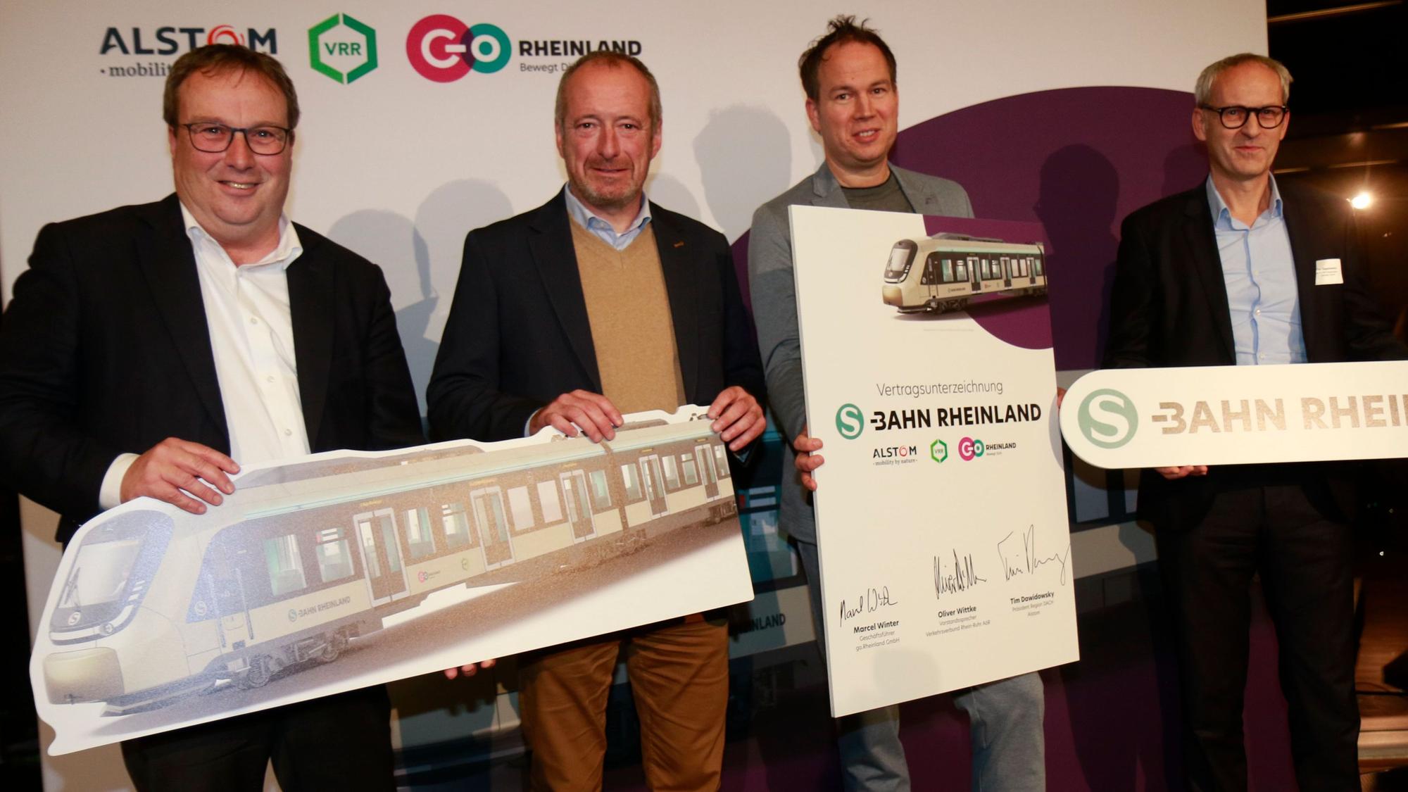 Zu sehen sind vier Männer, die Schilder hochhalten, auf denen auch S-Bahnen abgebildet sind.