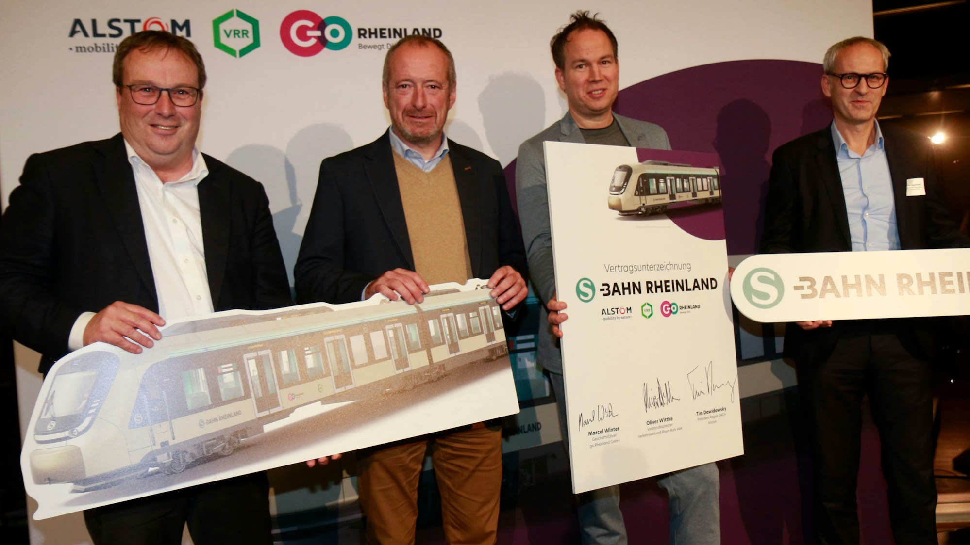 Zu sehen sind vier Männer, die Schilder hochhalten, auf denen auch S-Bahnen abgebildet sind.