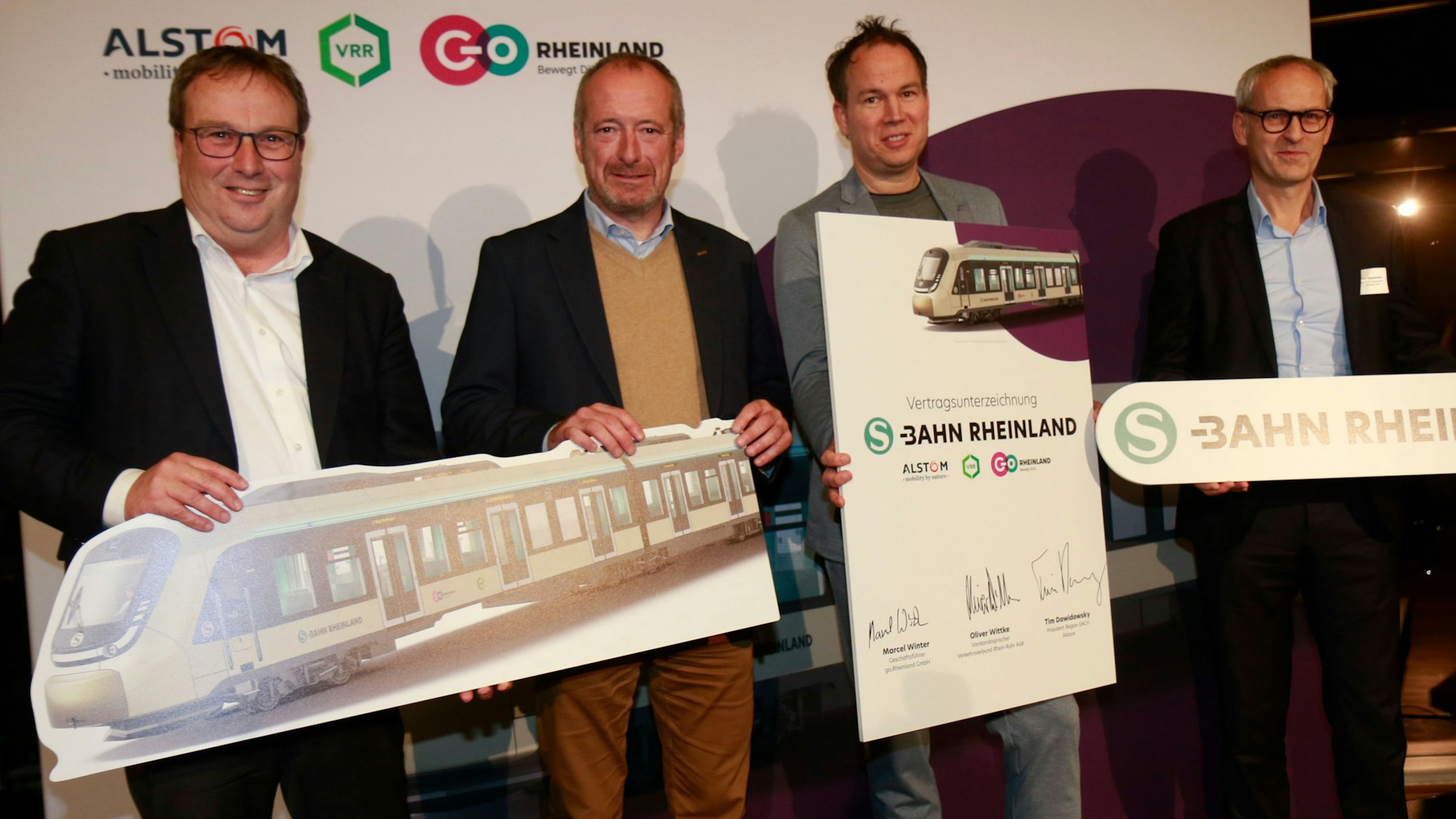 Zu sehen sind vier Männer, die Schilder hochhalten, auf denen auch S-Bahnen abgebildet sind.