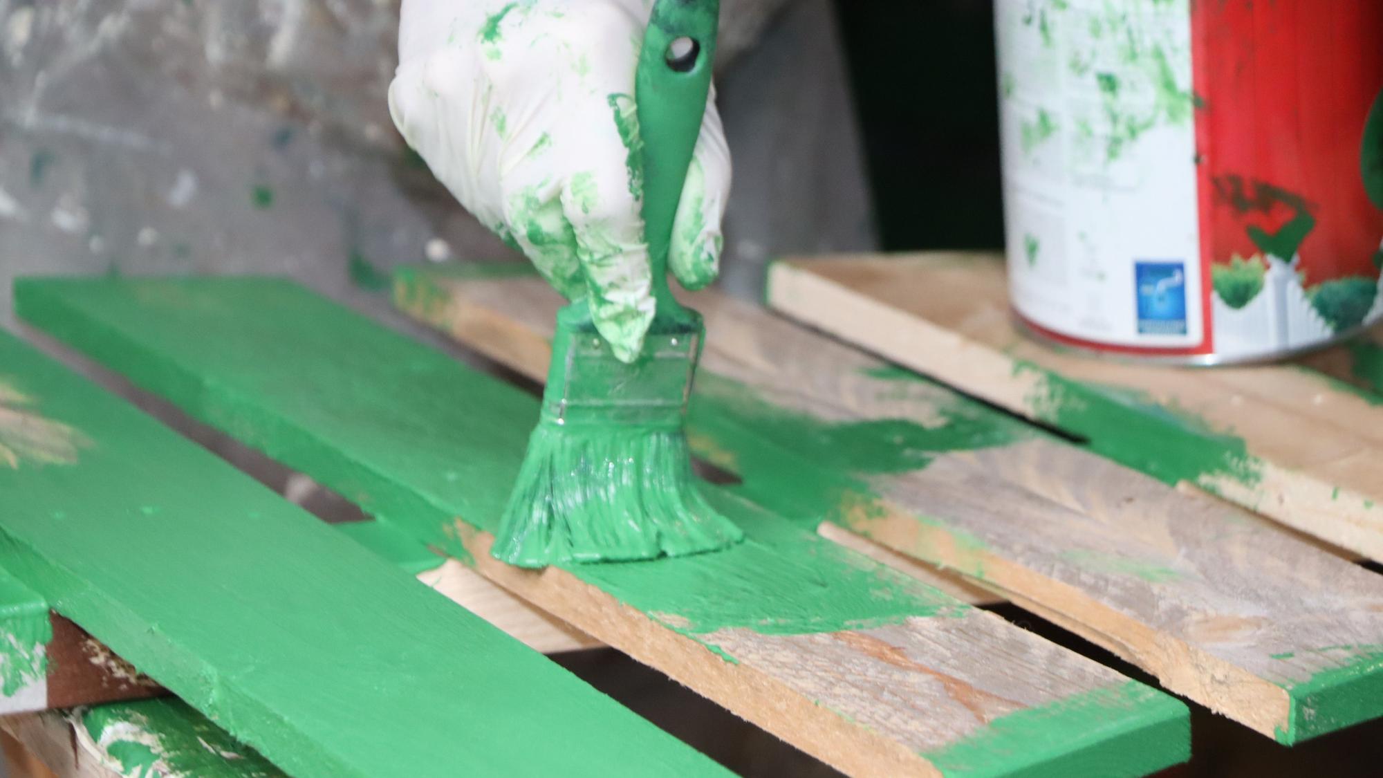 Auf dem Bild sind ein Pinsel mit grüner Farbe und Holzlatten zu sehen.