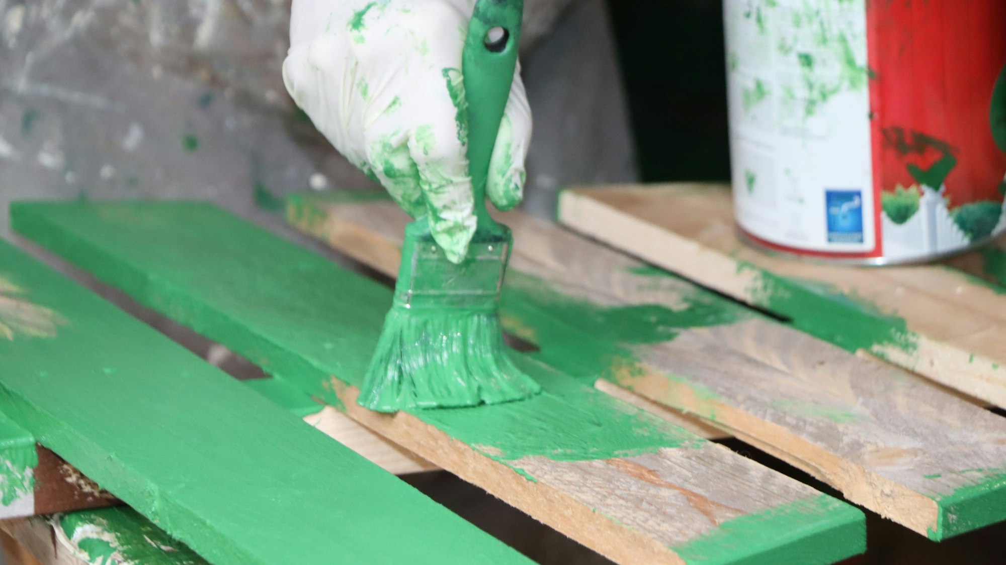 Auf dem Bild sind ein Pinsel mit grüner Farbe und Holzlatten zu sehen.