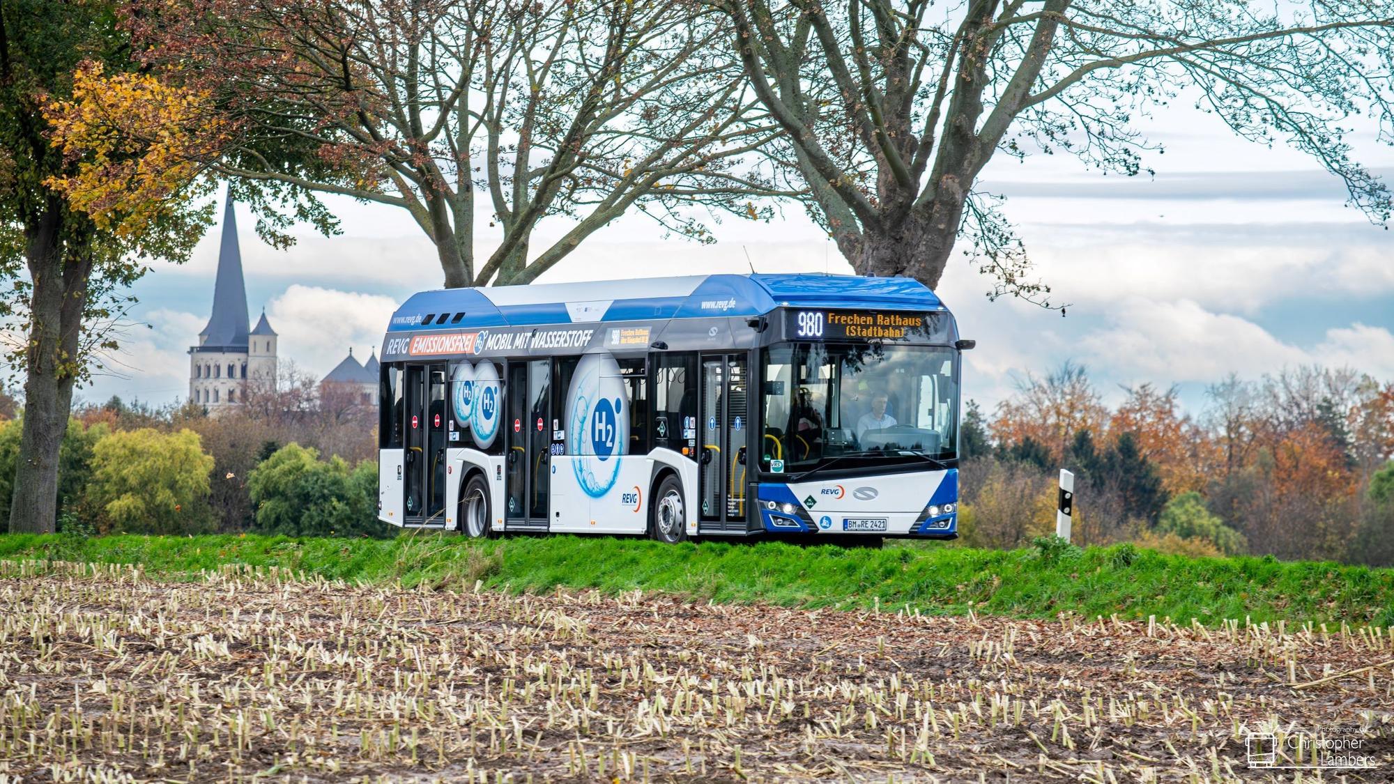 Auf dem Foto ist ein blau-weißer Bus zu sehen, der eine Landstraße befährt.