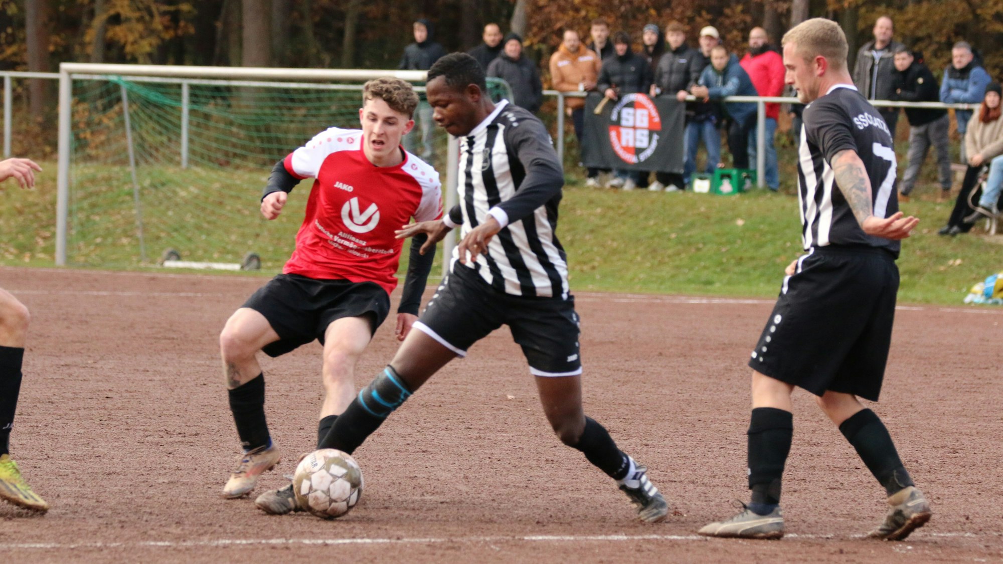 Zwei Fußballer im Zweikampf auf einem Aschenplatz. Im Hintergrund sind die Zuschauer zu erkennen.