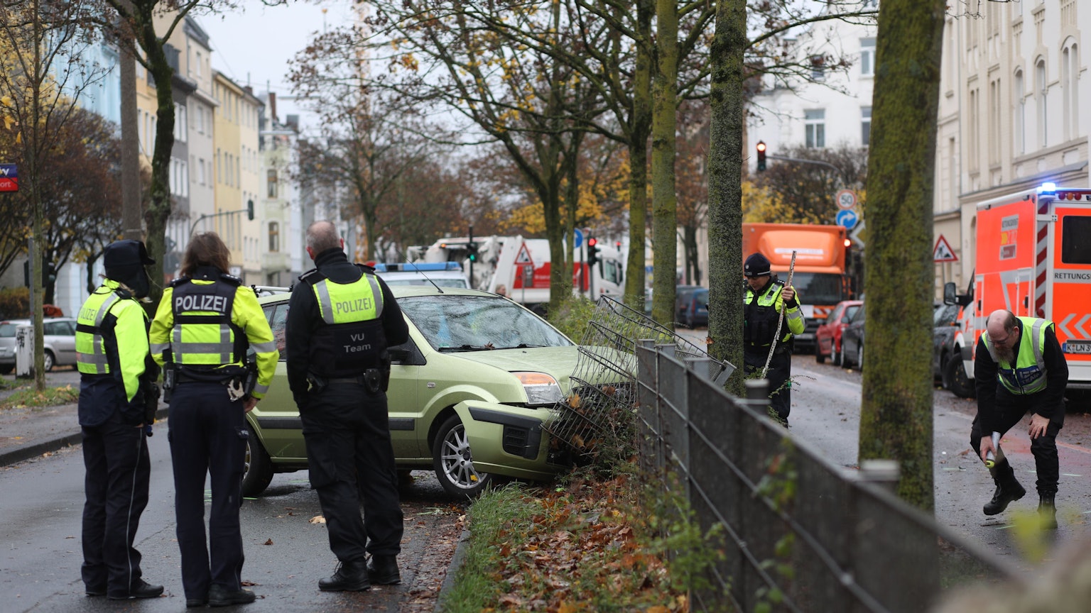 Ein Auto steht mit der Front im Mittelstreifen der Straße. Der Zaun ist beschädigt. Darum herum stehen Einsatzbeamte der Polizei.