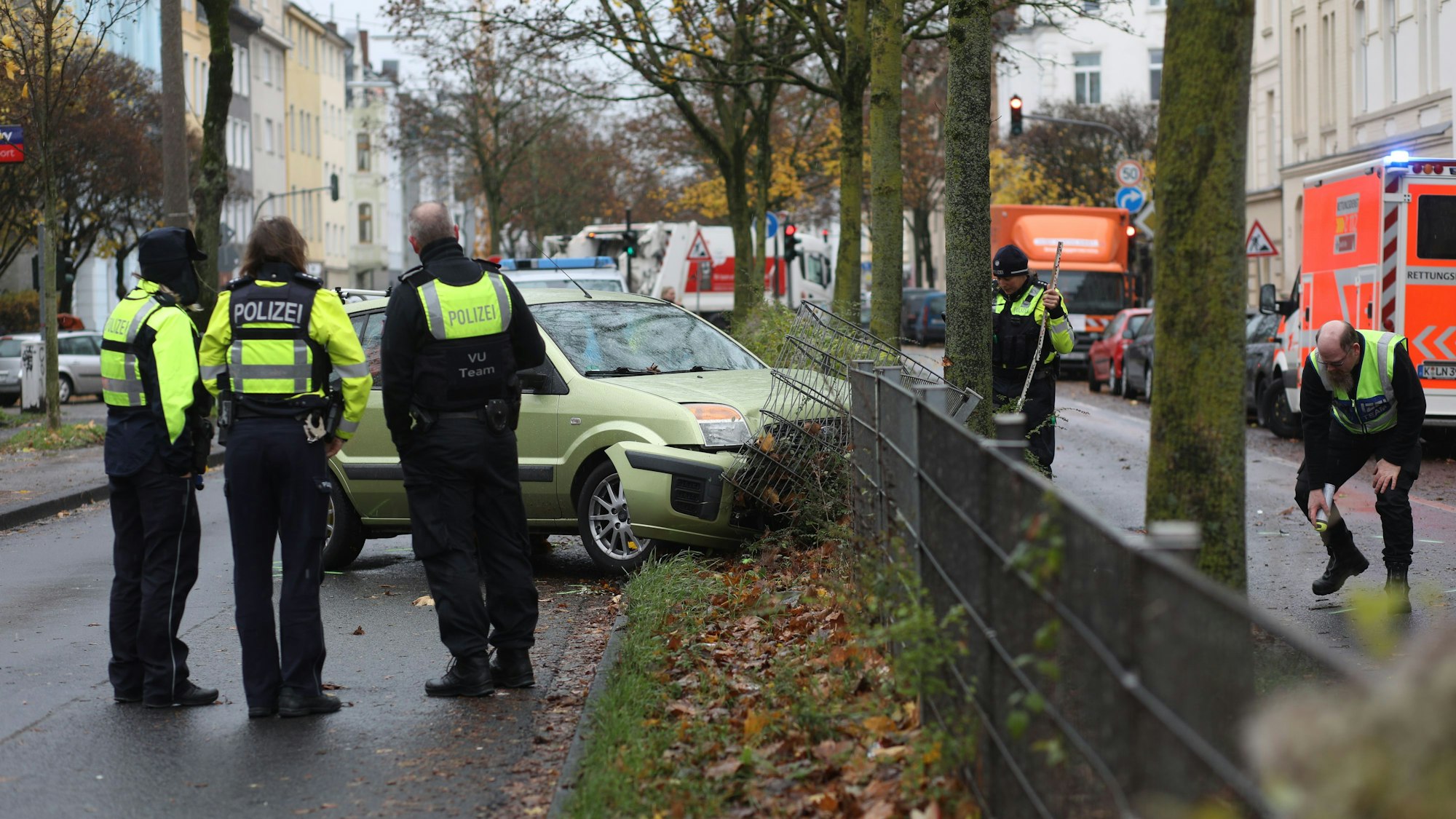 Ein Auto steht mit der Front im Mittelstreifen der Straße. Der Zaun ist beschädigt. Darum herum stehen Einsatzbeamte der Polizei.