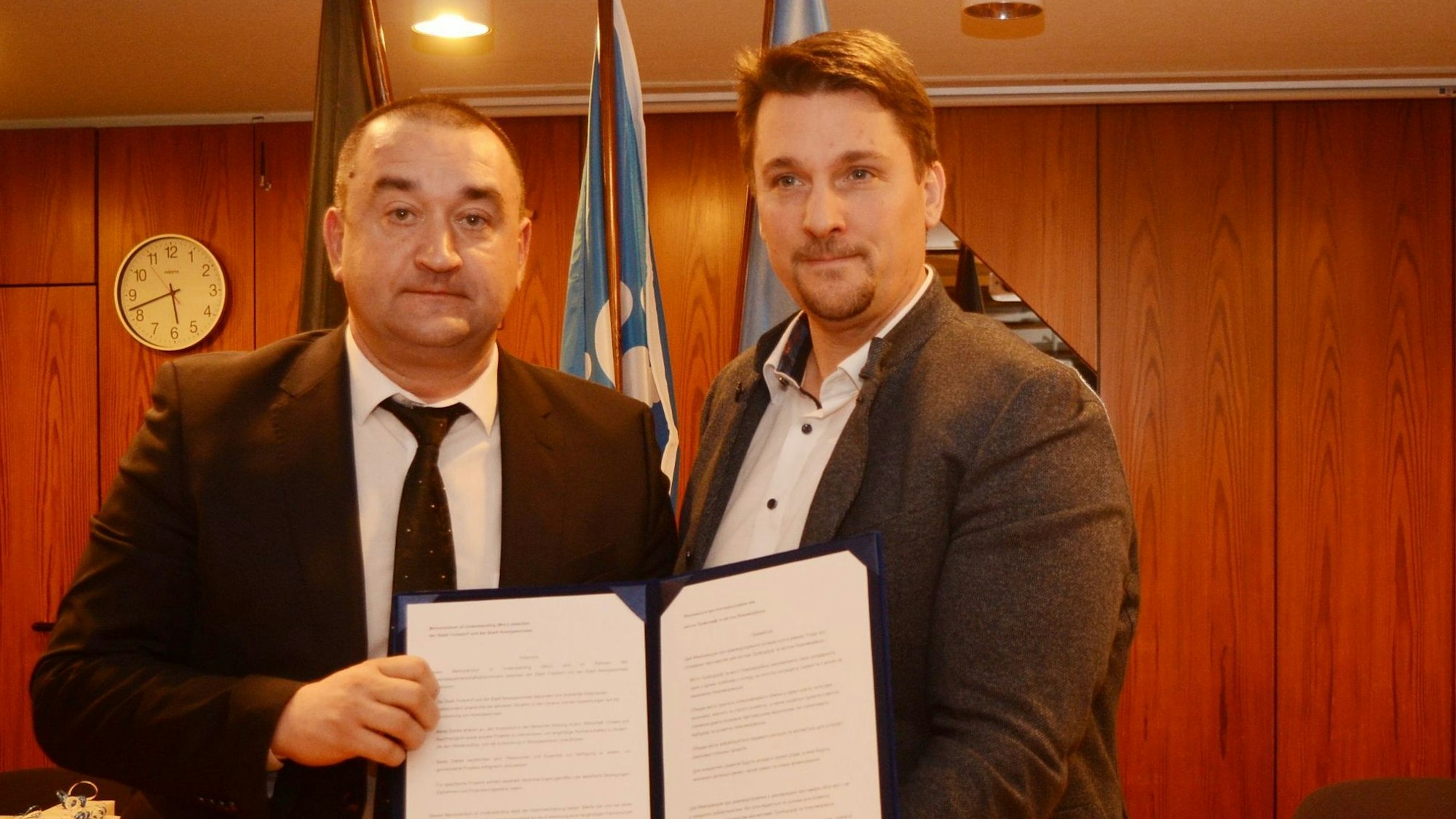 Zwei Männer im Anzug zeigen eine geöffnete Urkundenmappe.