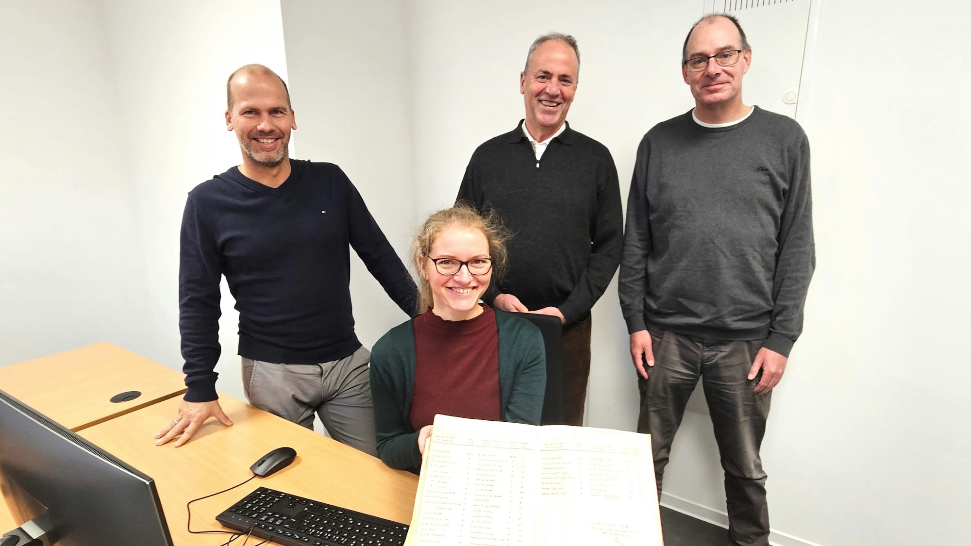 Markus Auel, Hermann-Josef Esser und Lothar Schatten stehen hinter der sitzenden Nicole Gutmann, die ein Familienbuch präsentiert.