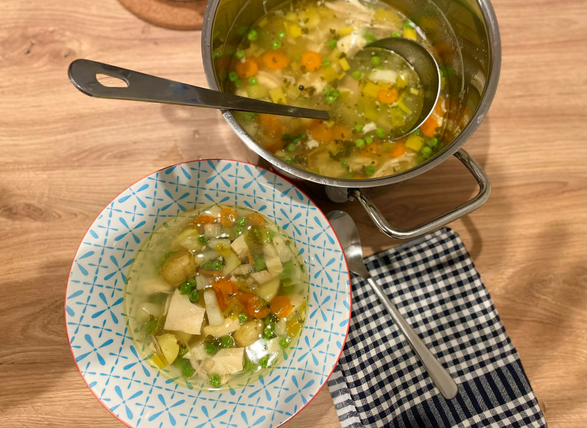 Hühnersuppe mit Eierstich, Erbsen, Möhren, Sellerie, Porree, Nudeln und Kartoffeln in einer Schüssel.