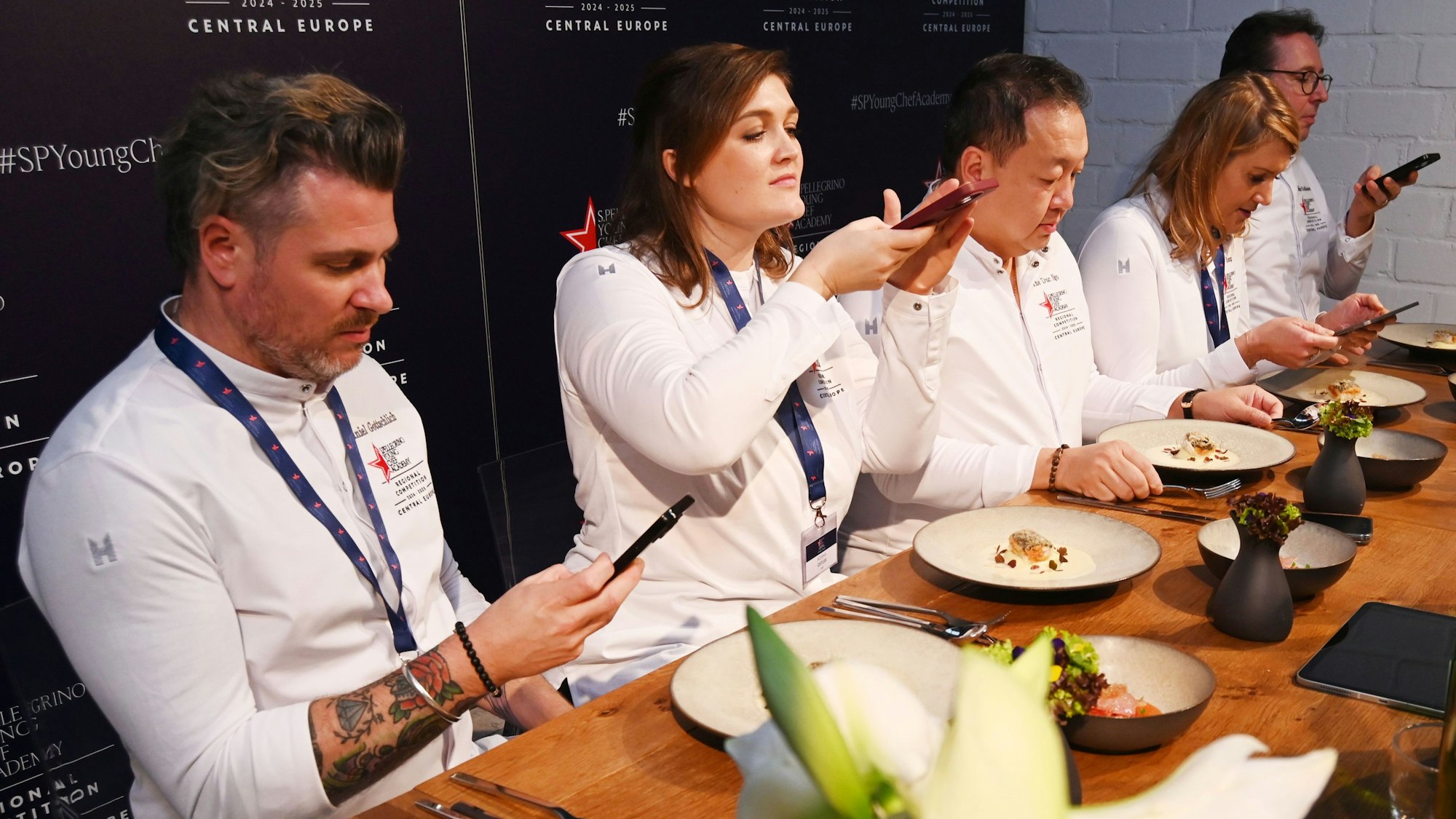 Fünf Köche sitzen nebeneinander und fotografieren die Teller vor sich.