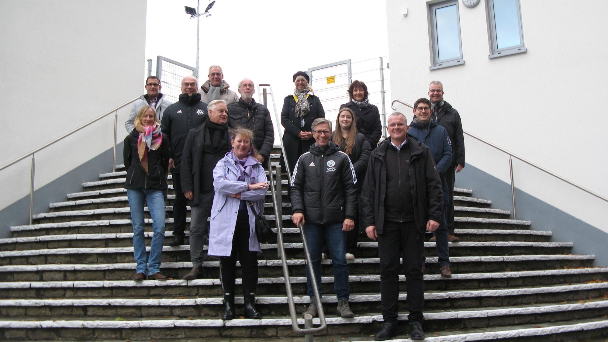 15 Personen stehen auf einer Treppe zwischen zwei Neubauten.