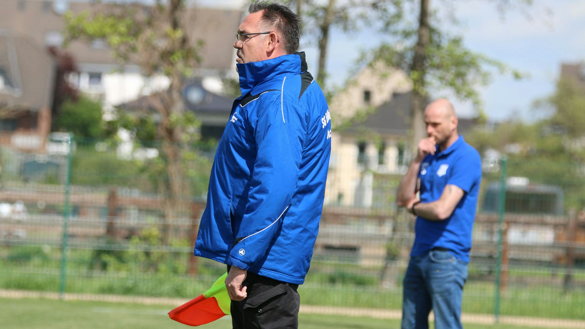 Zwei Trainer beobachten ein Fußballspiel. Einer von ihnen hält die Assistentenfahne in der Hand.