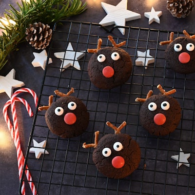 Kekse mit Augen, einer roten Schokolinse und Brezelgeweih liegen auf einem Gitter.