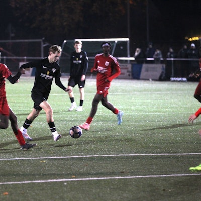 Ein Fußballer setzt zum Torschuss an, die Verteidiger kommen zu spät.