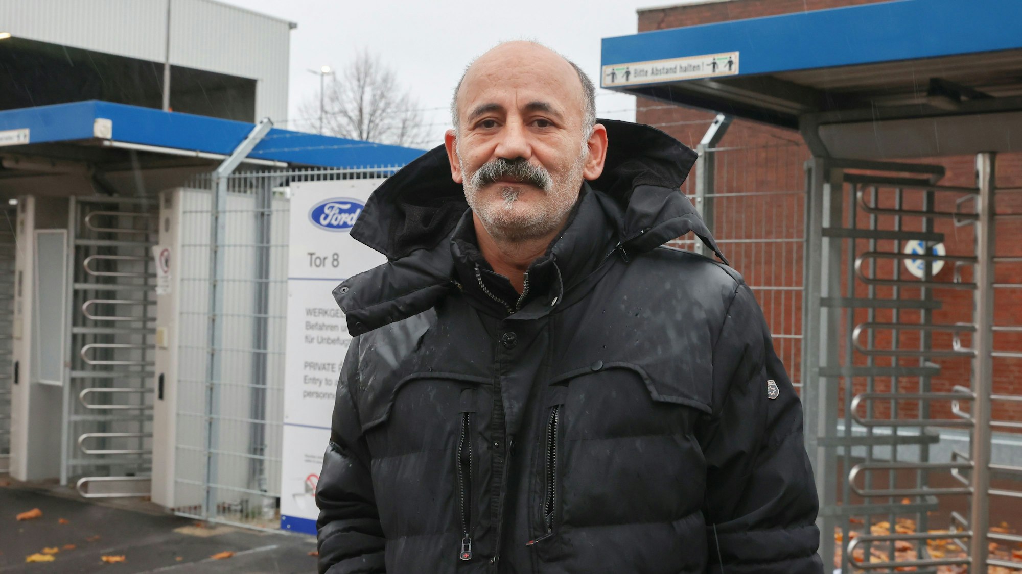 Senon Cicek (50) steht in einer schwarzen Winterjacke vor dem Eingang des Ford-Werks.
