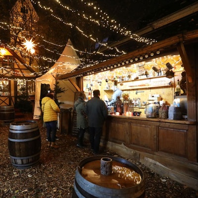 Eine Holzbude, an der es Getränke gibt, im Hintergrund eine Berghütte.
