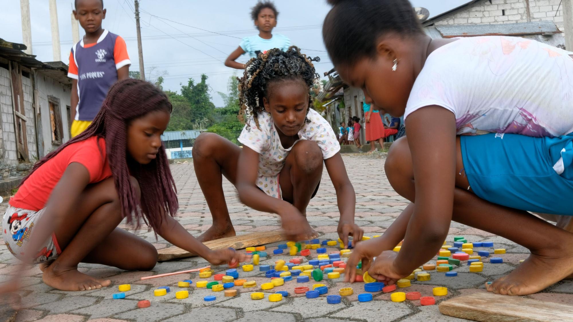Drei Mädchen spielen auf der Straße ein Spiel mit bunten Spielsteinen.