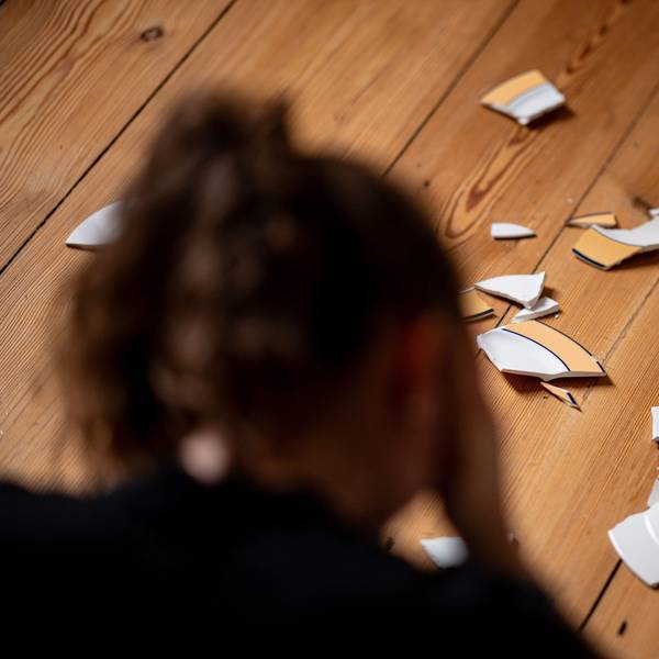 Eine Frau sitzt vor zerbrochenen Tellern, die auf dem Boden einer Wohnung liegen. Häusliche Gewalt gegen Frauen nimmt weiter zu.