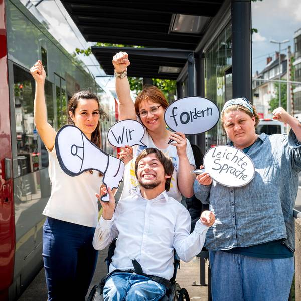 Auf dem Bild stehen Margarita Lüdtke Miró (v. l). Maximilian Westphal (vorne), Silke Degwitz und Dinah Köppen an einer KVB-Haltestelle. Sie halten Protestplakate.