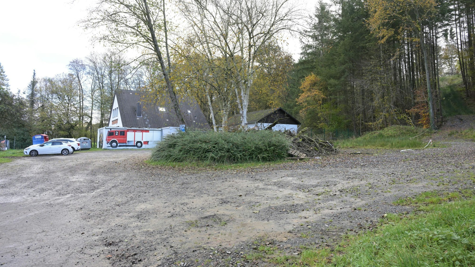 Ein unbefestigter Parkplatz, dahinter ein Feuerwehrhaus.