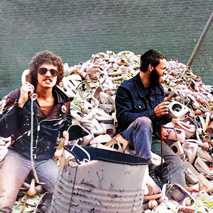 Drei Musiker sitzen mit Telefonen auf einem Müllberg mit Telefonen.