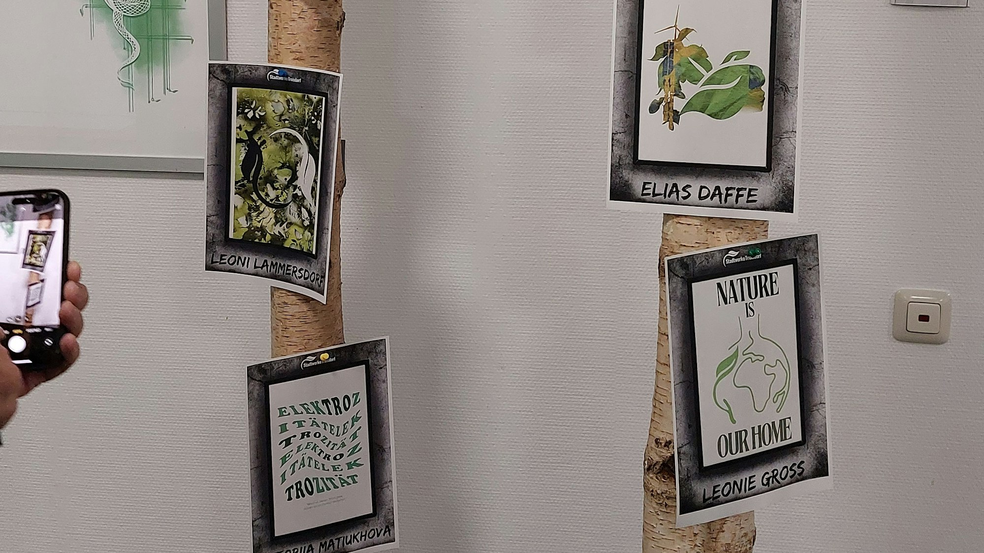 An zwei Baumstämmen sind Grafik-Entwürfe befestigt.