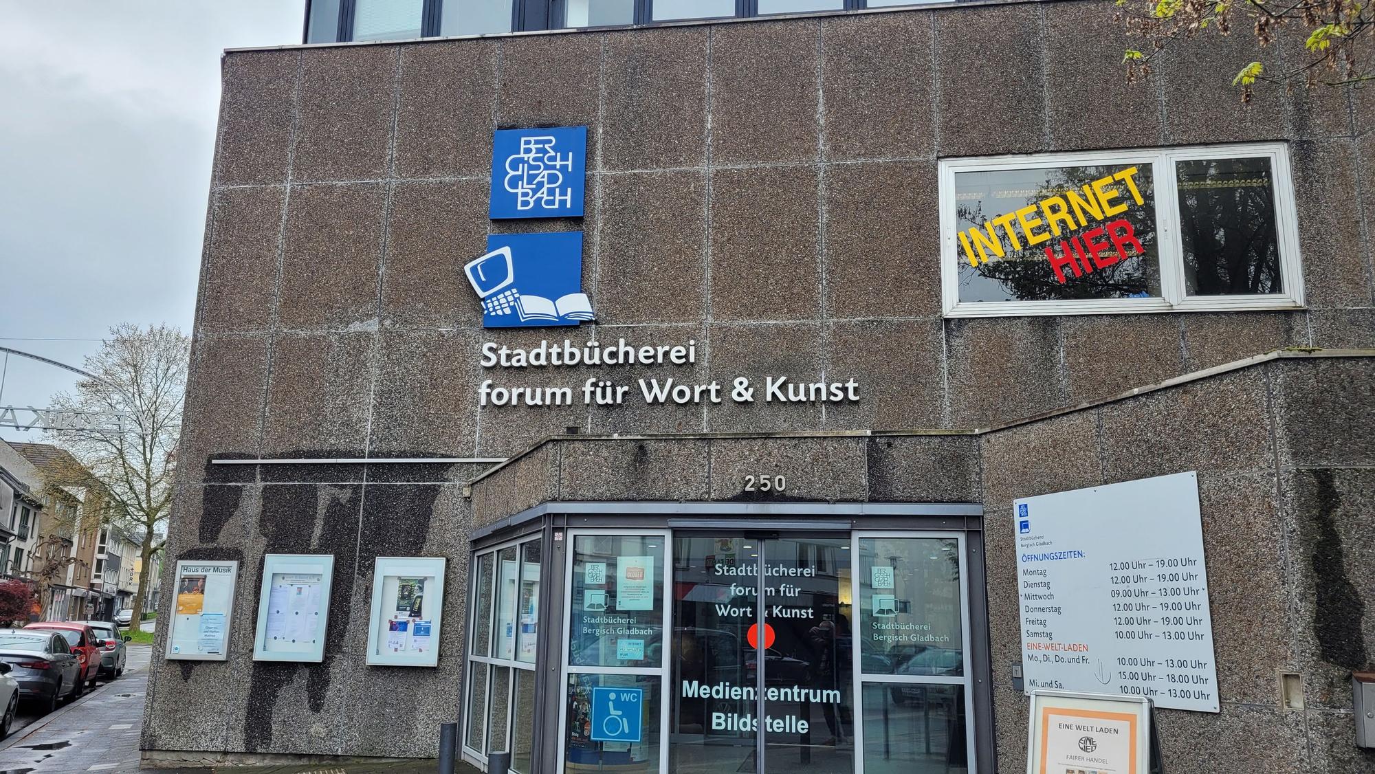 An der Waschbetonfassade hängen Plakate über dem Eingang.