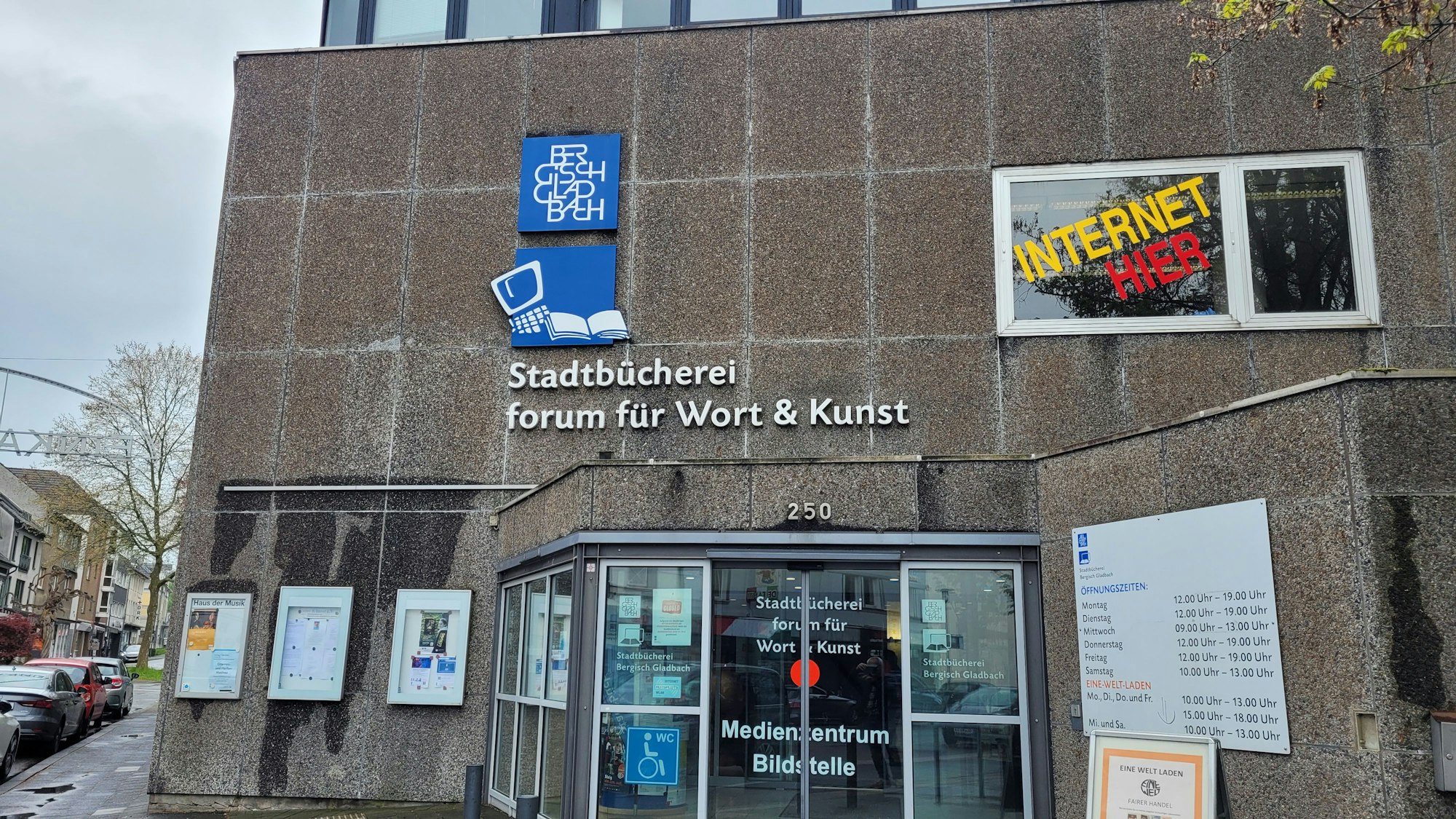 An der Waschbetonfassade hängen Plakate über dem Eingang.