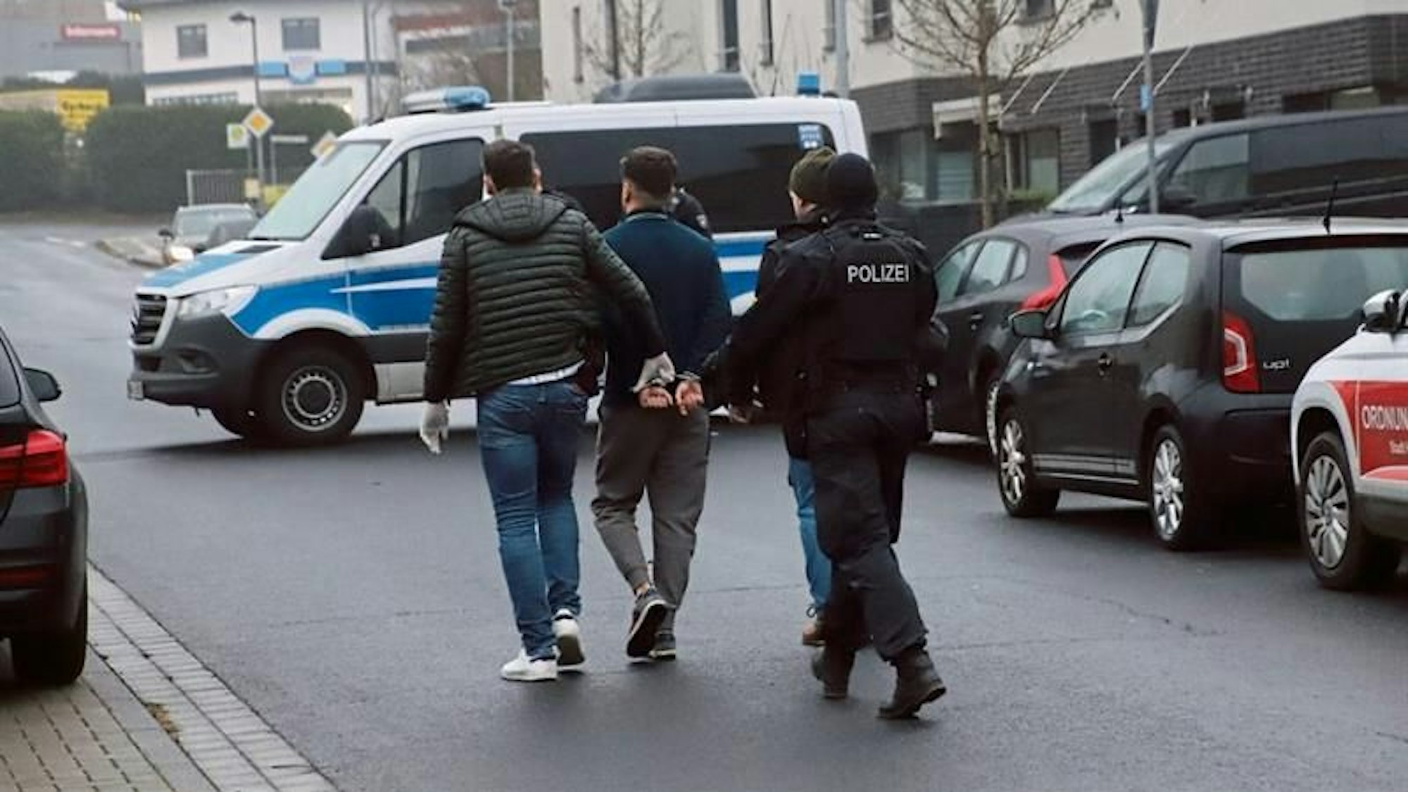 Die Polizei führt bei der Razzia wegen gefälschten Sprachzertifikaten in Hennef-Hossenberg einen Verdächtigen ab.