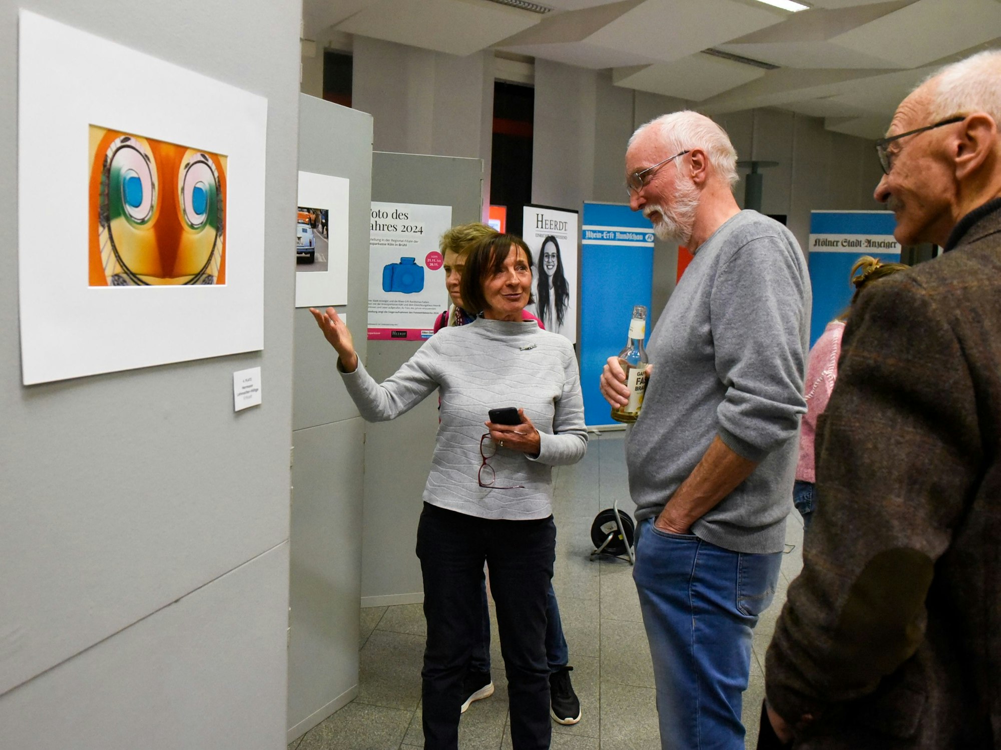 Die Gewinner des Fotowettbewerbs unterhalten sich vor einer Wand, auf denen die Gewinnerfotos angebracht sind.