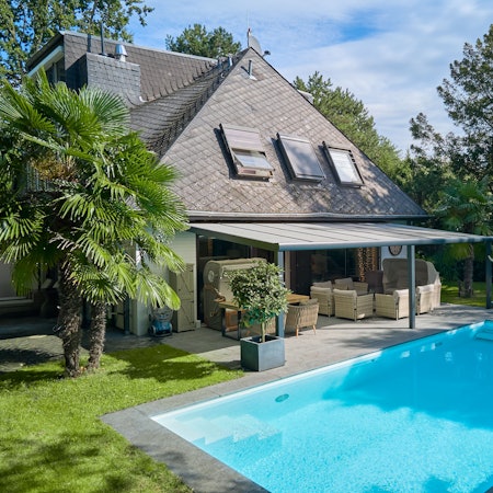 Eine Villa mit schwarzem Dach, davor eine Terrasse und ein Pool.