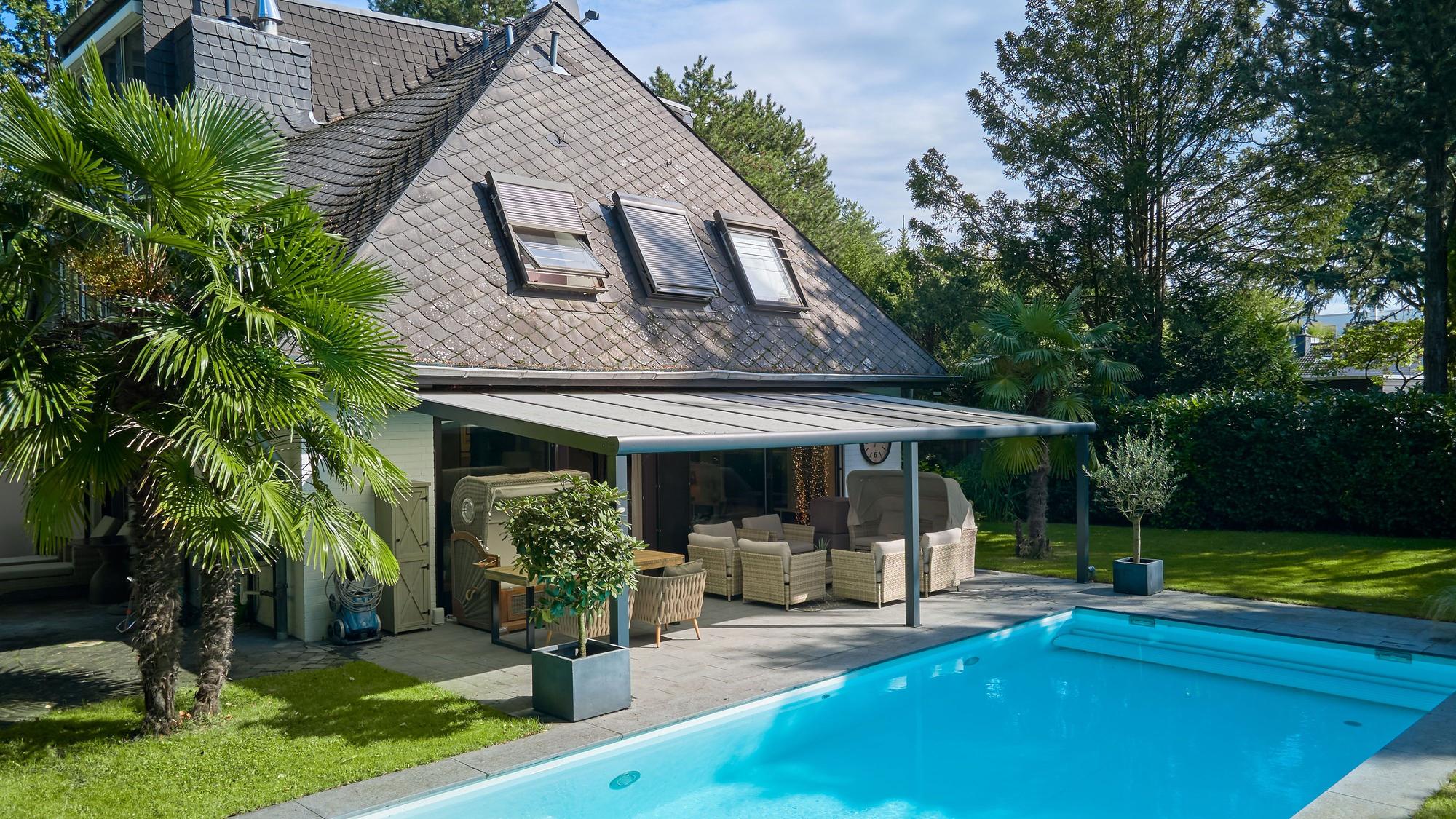 Eine Villa mit schwarzem Dach, davor eine Terrasse und ein Pool.
